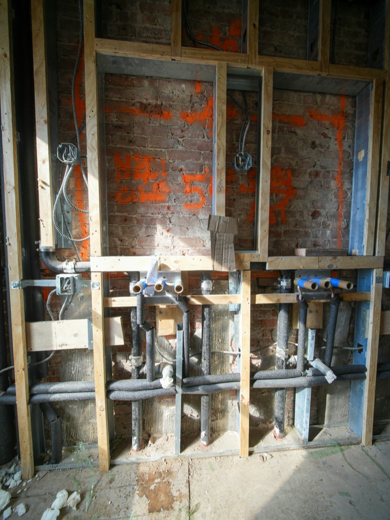Exposed pipes and wiring inside a brick wall during a renovation.